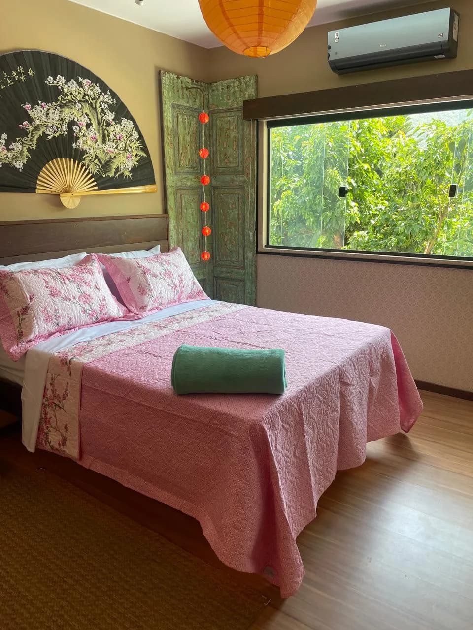 Loft Okinawa: Leque japonês na parede, rosa e verde, janela emoldurando a mata.